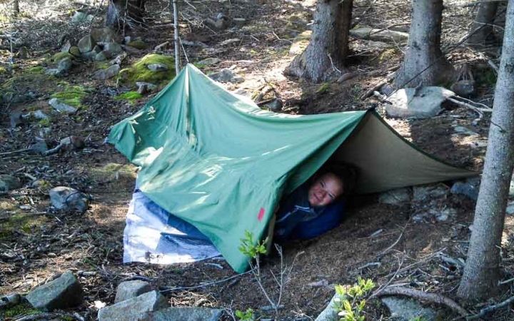 a person smiles while laying under a tarp in the woods on an outward bound expedition 
